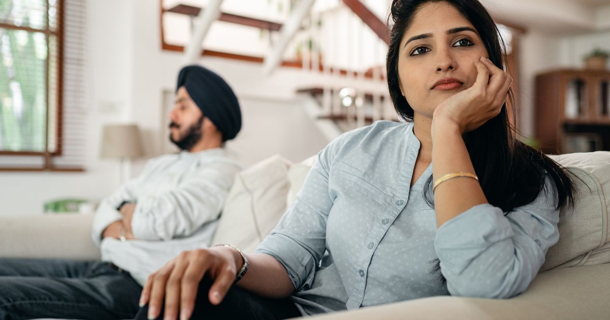 Young Indian couple sitting on different sides of couch and ignoring each other after arguing at home