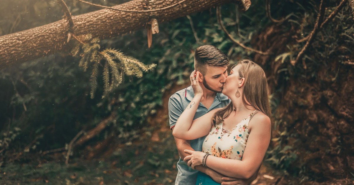 A couple shares a romantic kiss surrounded by lush forest scenery, adding a touch of nature and intimacy.