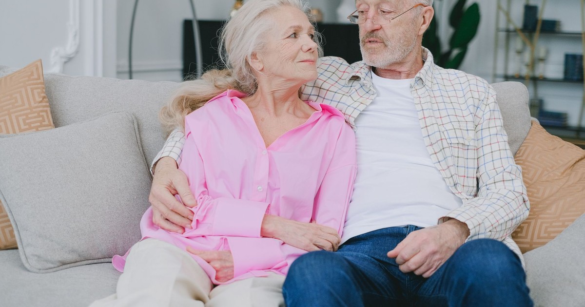 A senior couple lovingly embraces while sitting on a cozy sofa in their living room.