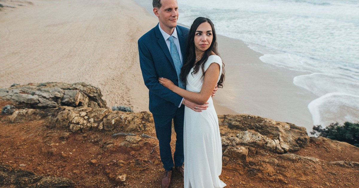 A couple in wedding attire embraces on a picturesque seaside cliff at sunset, symbolizing love.