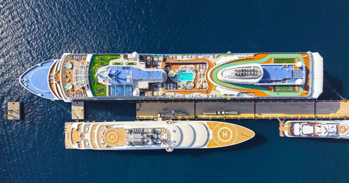 Top-down view of two luxurious cruise ships moored at a sunny port, showcasing pools and helipads.
