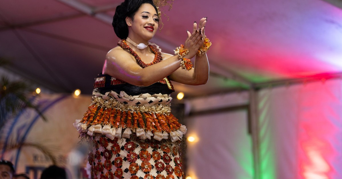 A woman performs a traditional Polynesian dance, adorned in vibrant cultural attire under festive lighting.