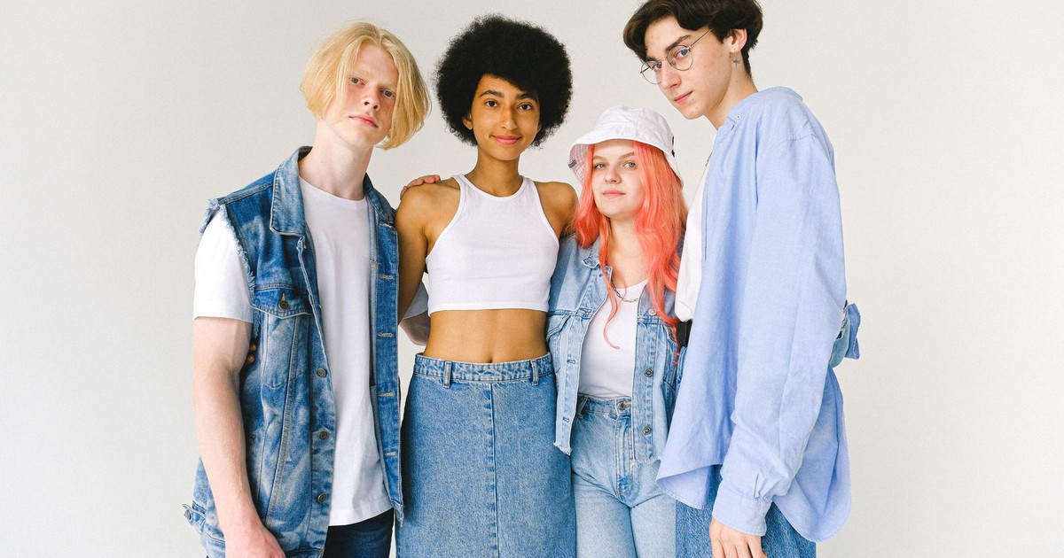 Content diverse teenager friends wearing denim clothes standing against white background hugging and looking at camera