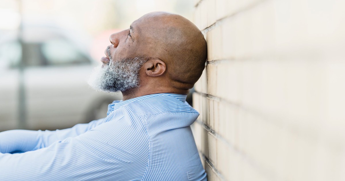 Side view of a thoughtful man with a beard leaning against an outdoor brick wall.