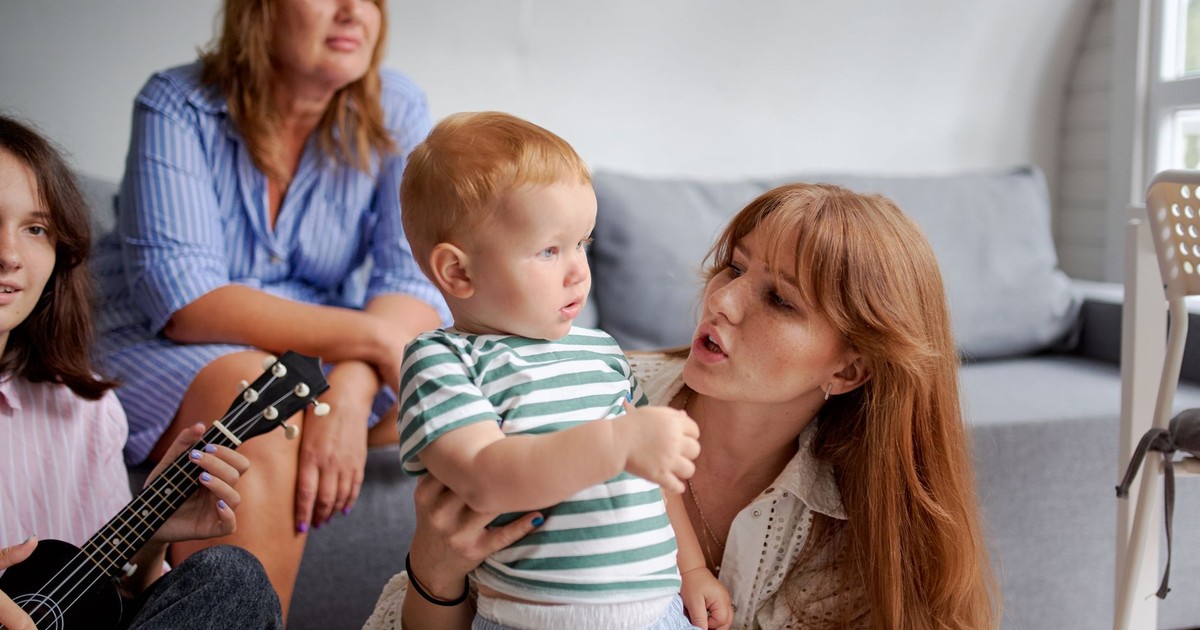 Women with toddler child near crop grandmother and sister playing ukulele while spending time together on weekend