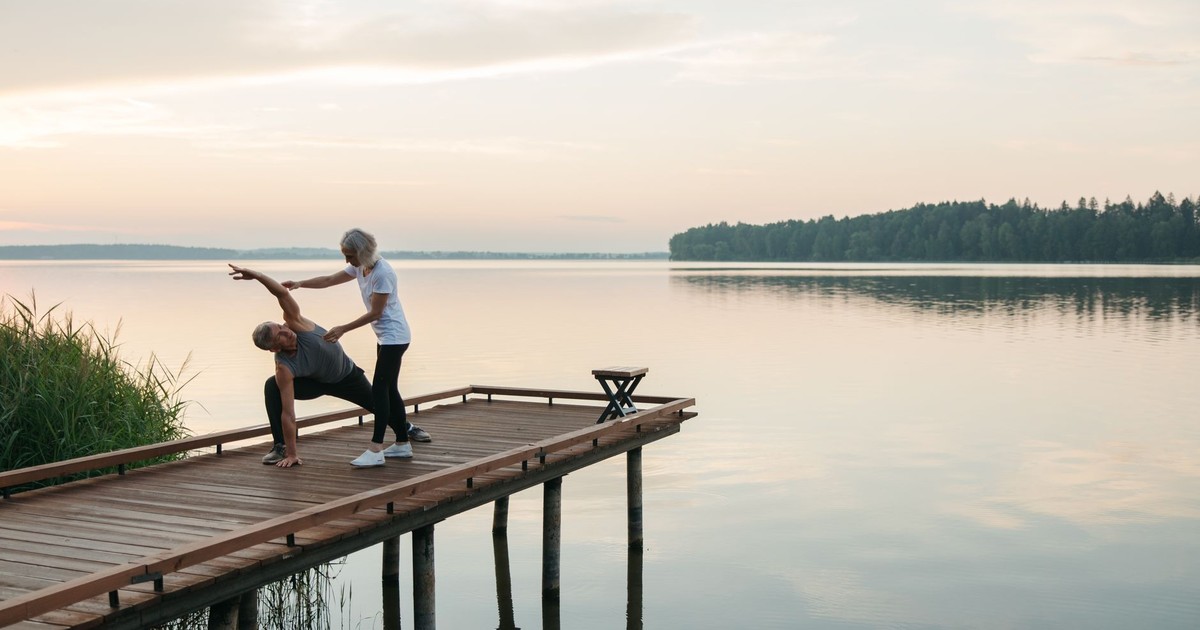 Senior adults practicing yoga on a wooden dock by a serene lake during sunrise, promoting health and mindfulness.