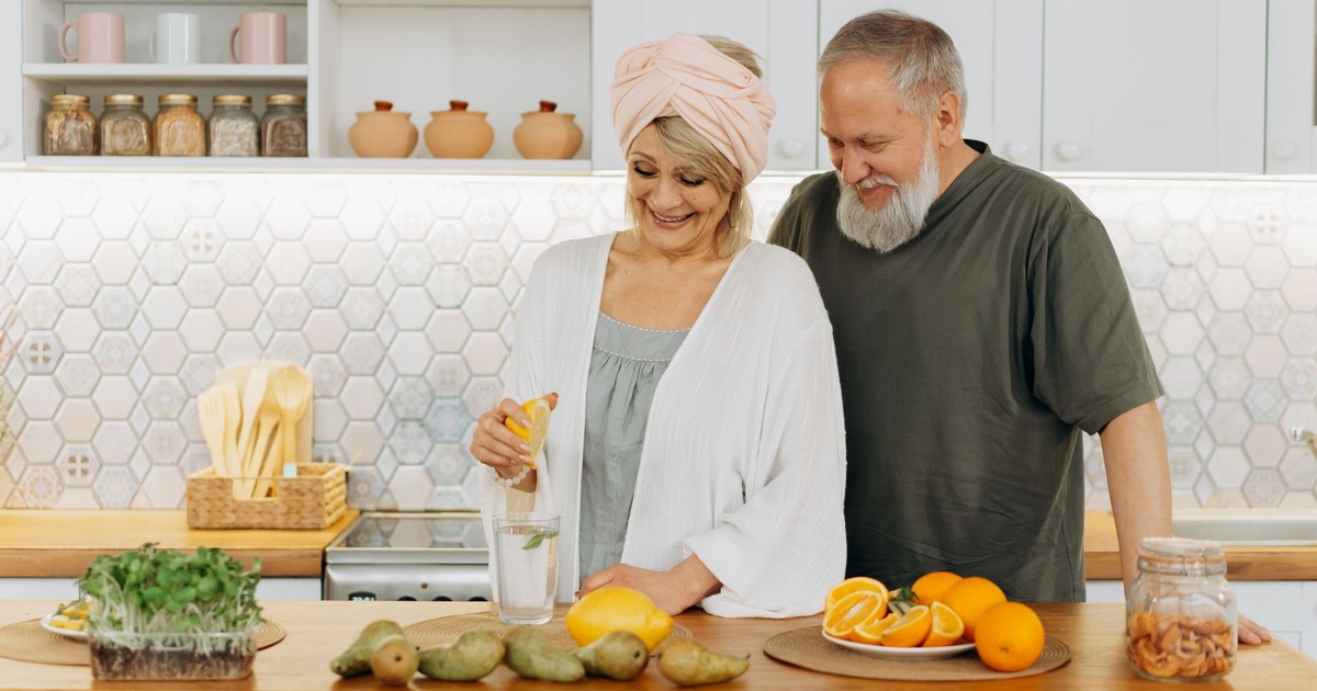 Senior couple squeezing citrus in a bright kitchen setting, promoting healthy living and joyful togetherness.