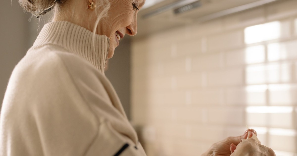 Elderly woman smiling while preparing a meal in her cozy kitchen indoor setting.