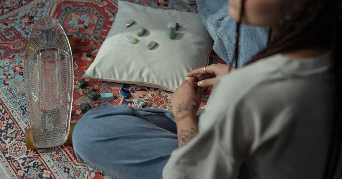 Woman seated on a rug with crystals and a glass skateboard, indoors.