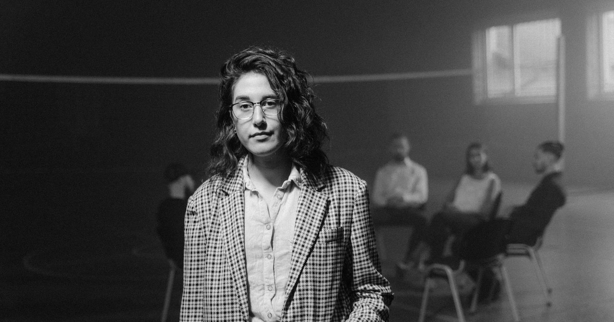 Monochrome image of a woman standing with a support group meeting in the background.
