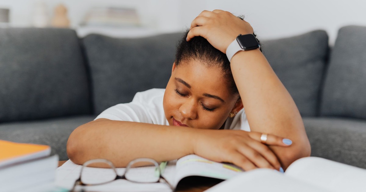 A woman rests on textbooks, exhausted from studying in her cozy living room environment.