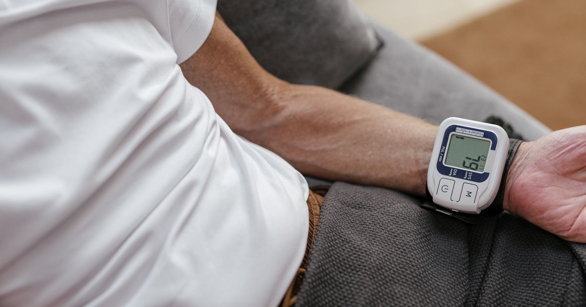 Adult man using a wrist blood pressure monitor to measure blood pressure at home.