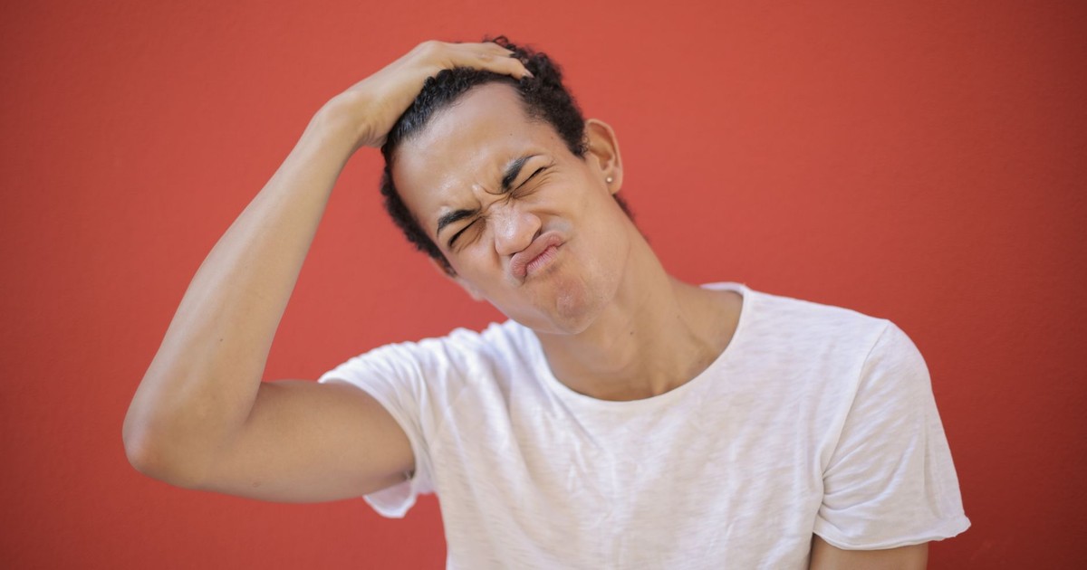 Happy ethnic with piercing putting hand on head and frowning face while standing against red background