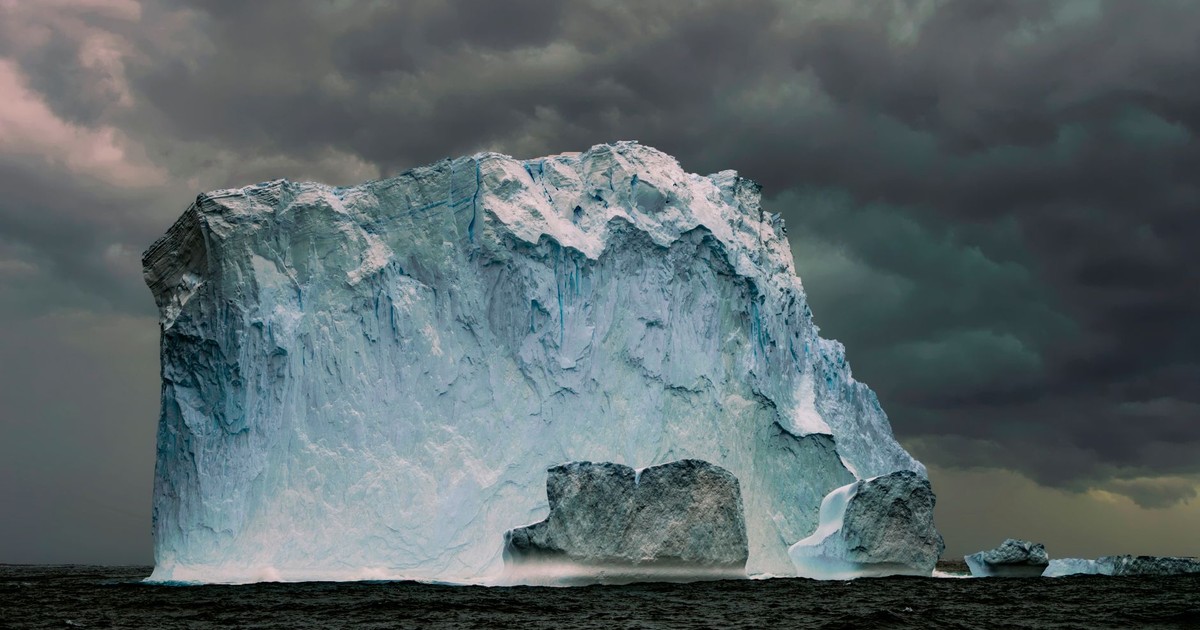 A massive iceberg floating in the sea with dramatic storm clouds overhead, showcasing nature's power.