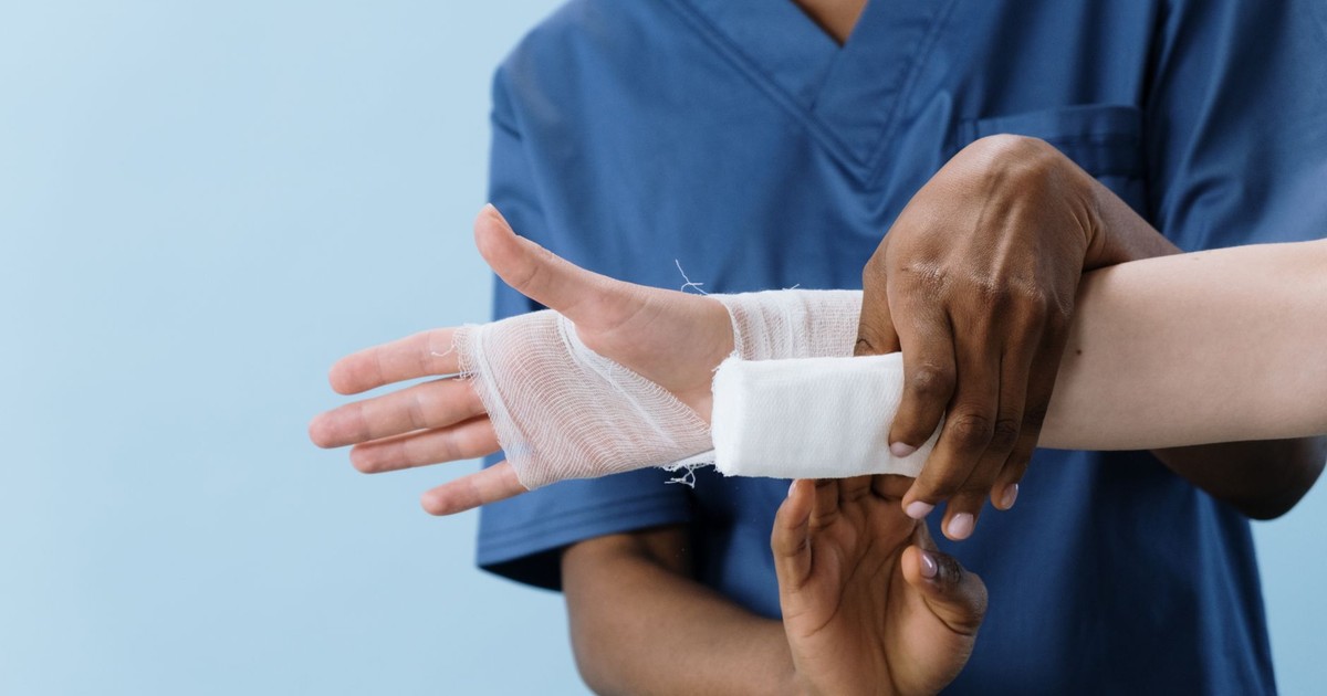 A medical professional carefully wrapping a bandage around an injured person's hand.