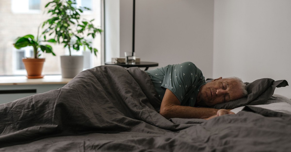 Senior man resting peacefully on a bed inside a room with natural light and plants.