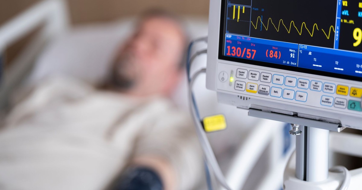 Patient in hospital bed with heart monitor showing blood pressure and heart rate.