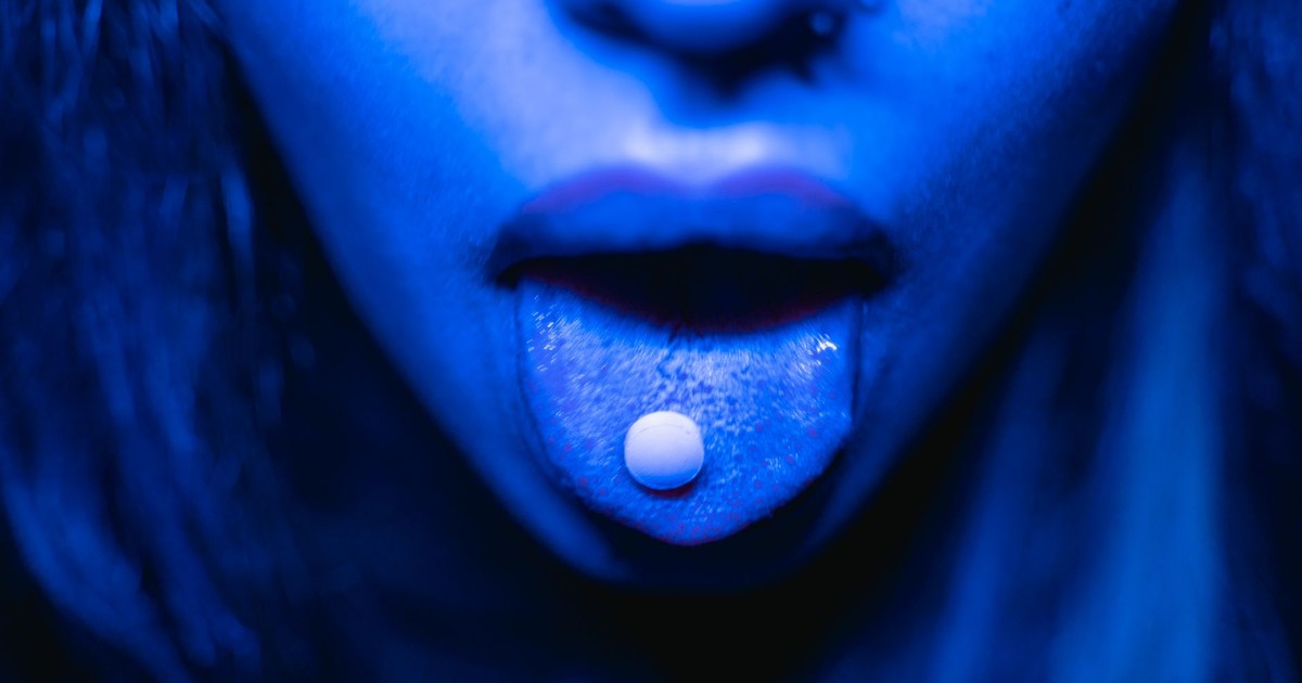 Dramatic close-up of a person with a tablet on their tongue in blue lighting.