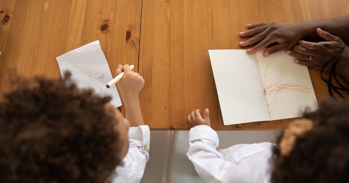Two kids with curly hair drawing together at a wooden table, enjoying creative time.
