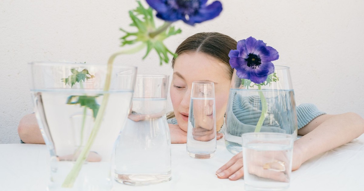 A young woman gazes at vibrant anemone flowers in clear vases filled with water.