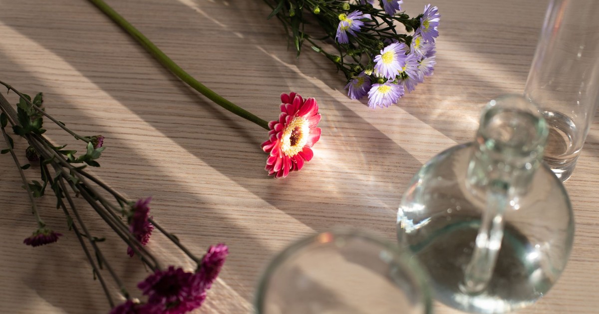 From above of fresh gerbera placed on wooden table near bunches of globe amaranth and aster flowers composed with glass vases
