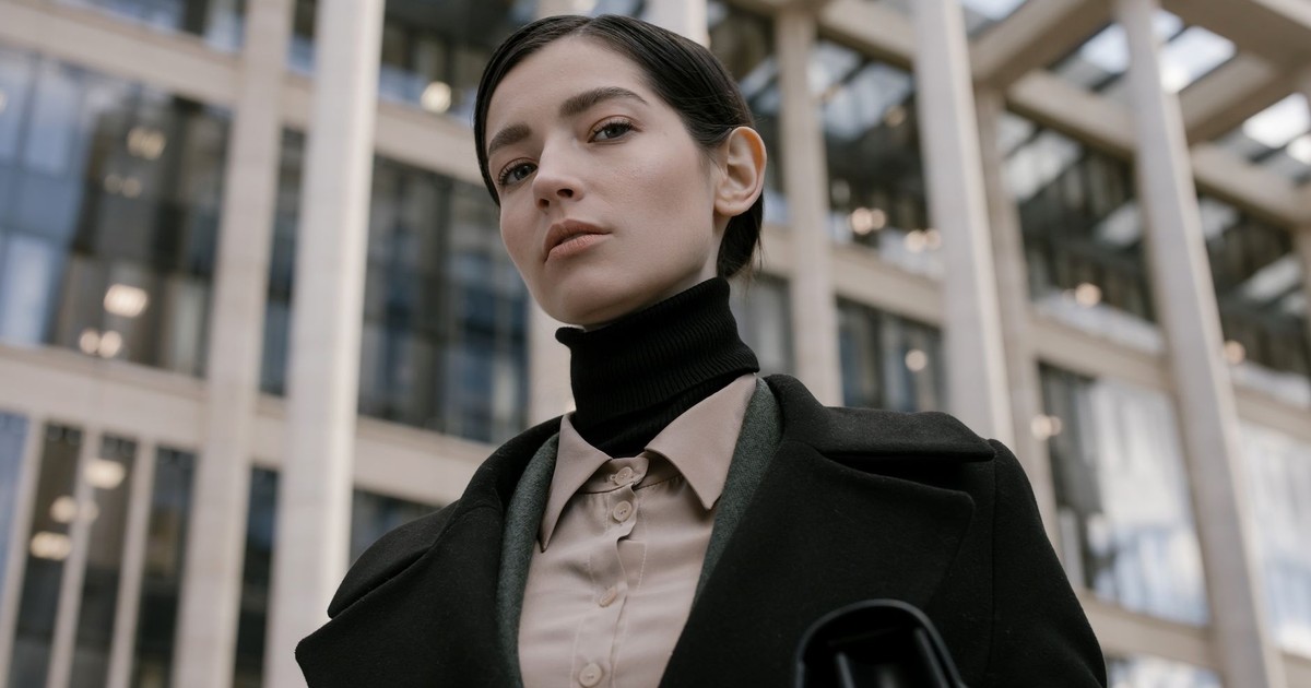 A fashionable young woman in professional attire with urban architecture background.
