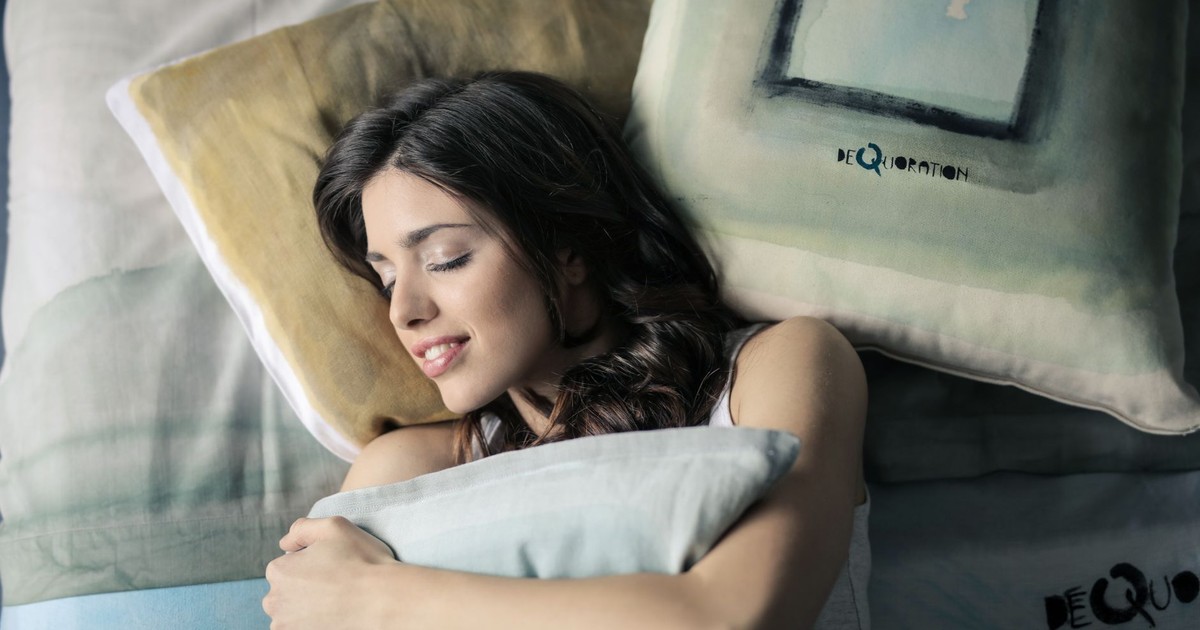Woman peacefully sleeping in bed, hugging a pillow with a contented smile.