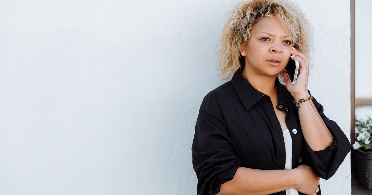 Casual woman with curly hair in a black shirt talking on the phone outdoors.
