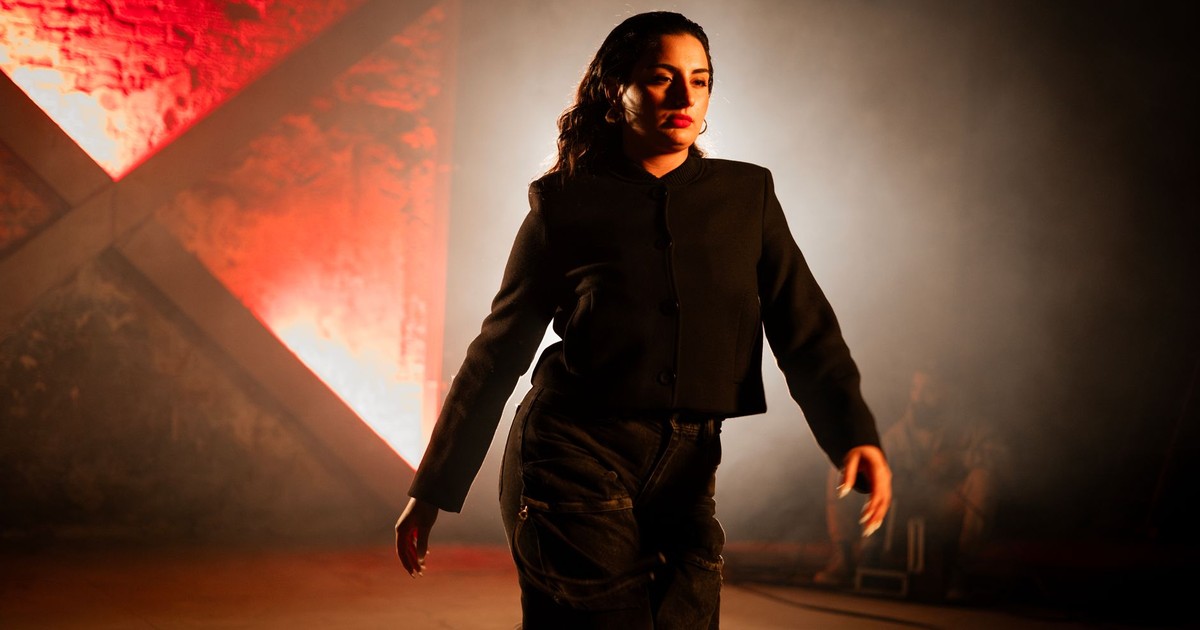 A woman walks confidently in a red-lit industrial setting, creating a dramatic atmosphere.