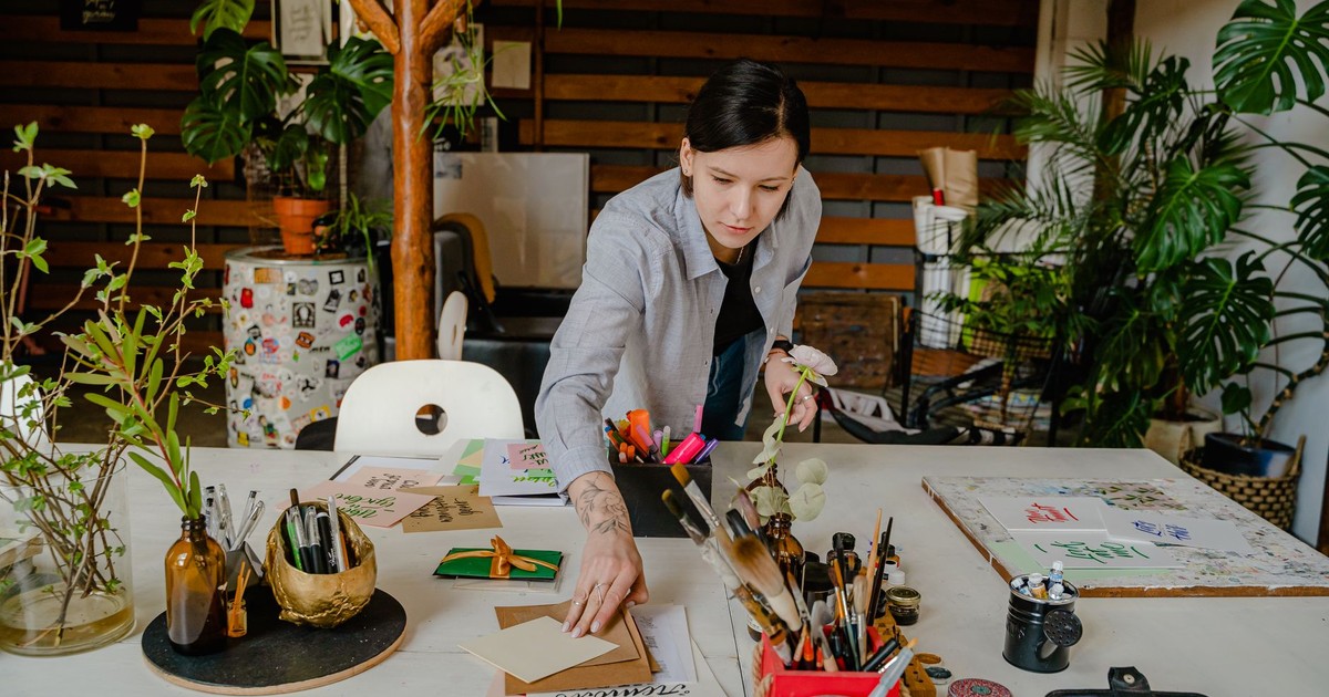 A woman organizing art supplies on a desk in a creatively decorated indoor workspace.