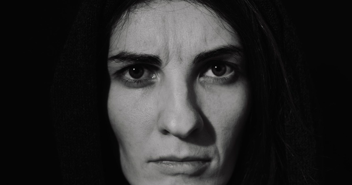 Close-up black-and-white portrait of a woman with a serious expression, wearing a hood.