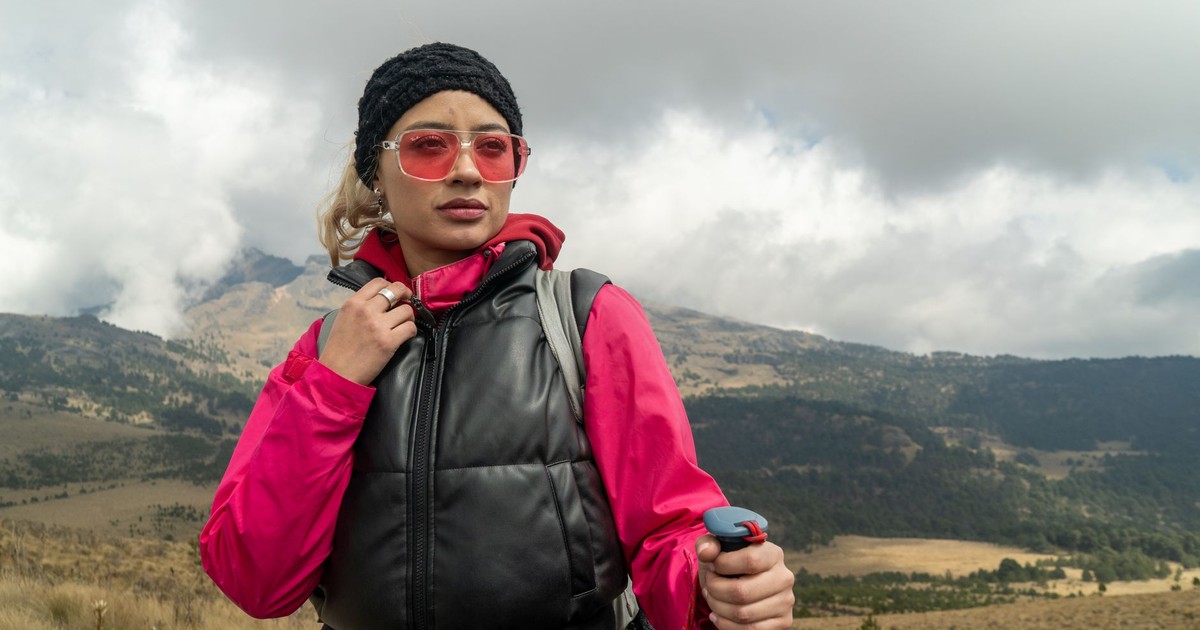 Woman in vibrant hiking gear explores a cloudy, mountainous landscape. Adventure awaits.