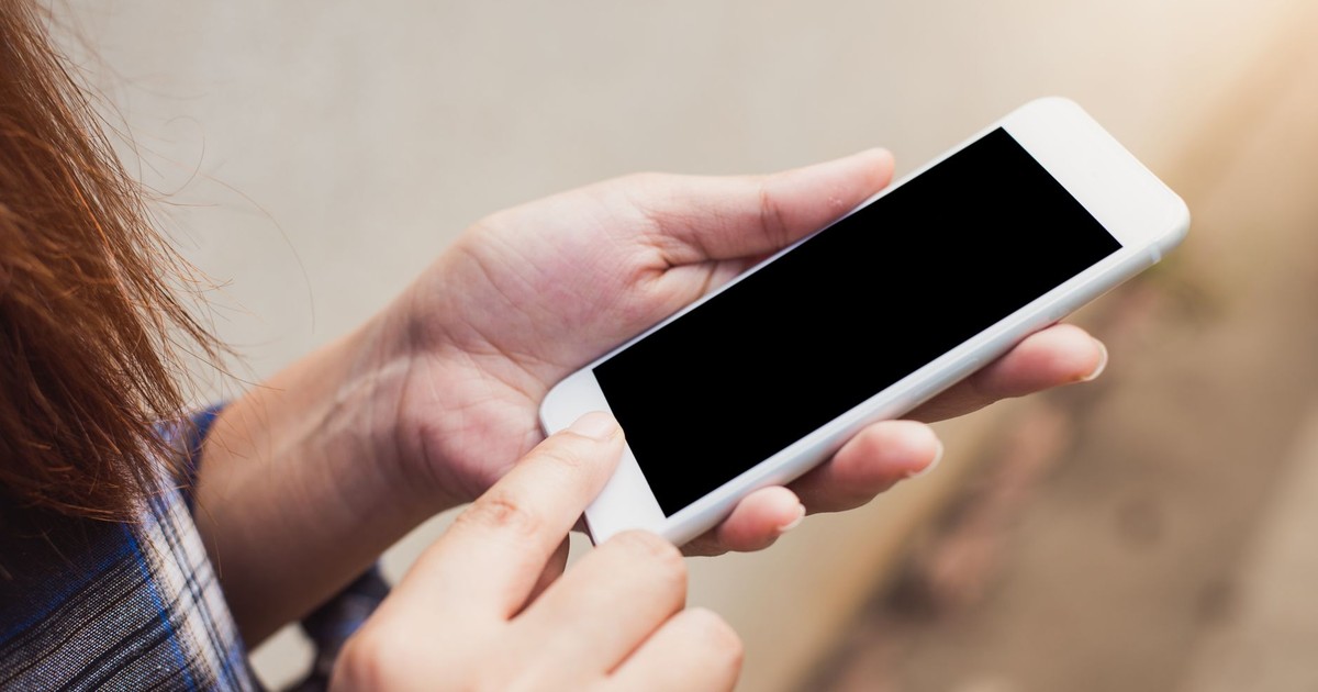 Person holding and using a smartphone outdoors, focusing on hands and screen.