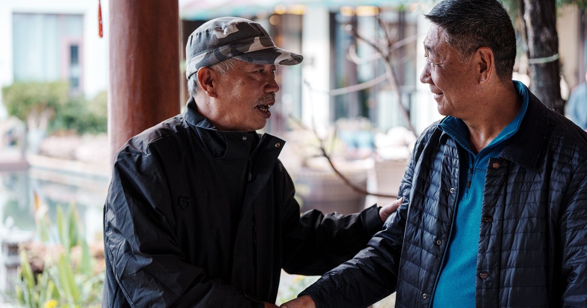 Two older men greet each other warmly outside in a relaxed setting.