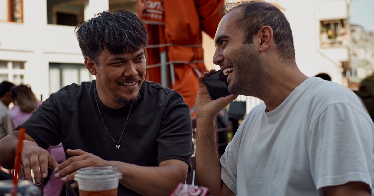 Two men smiling and chatting over drinks at an outdoor café.