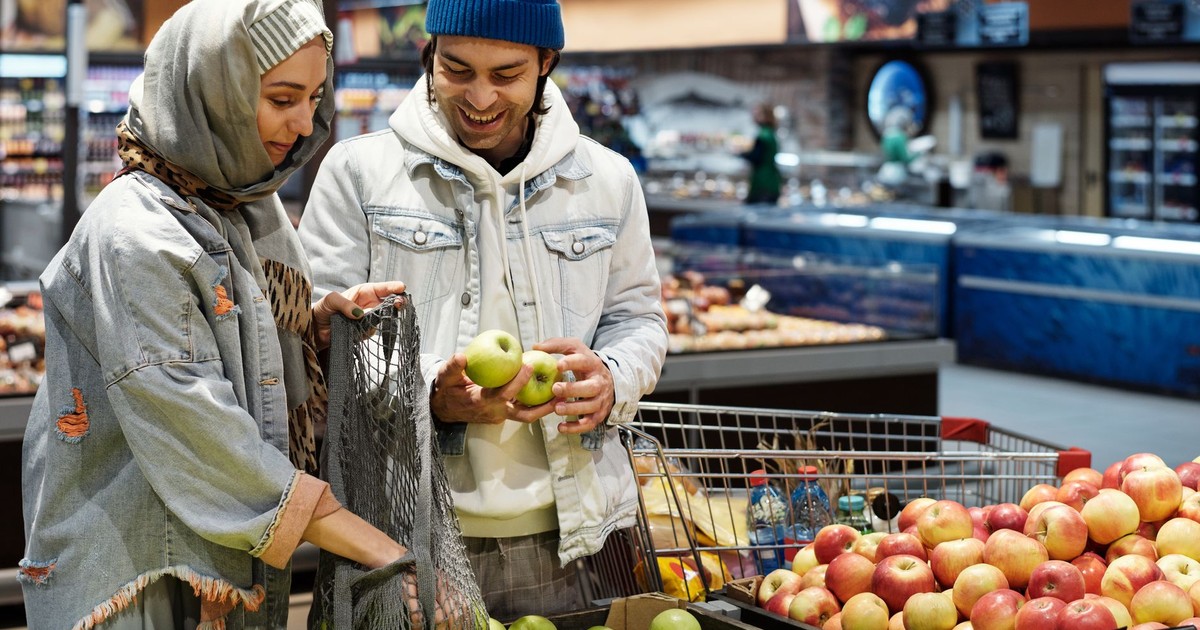 A smiling couple selects apples together in a vibrant supermarket setting.