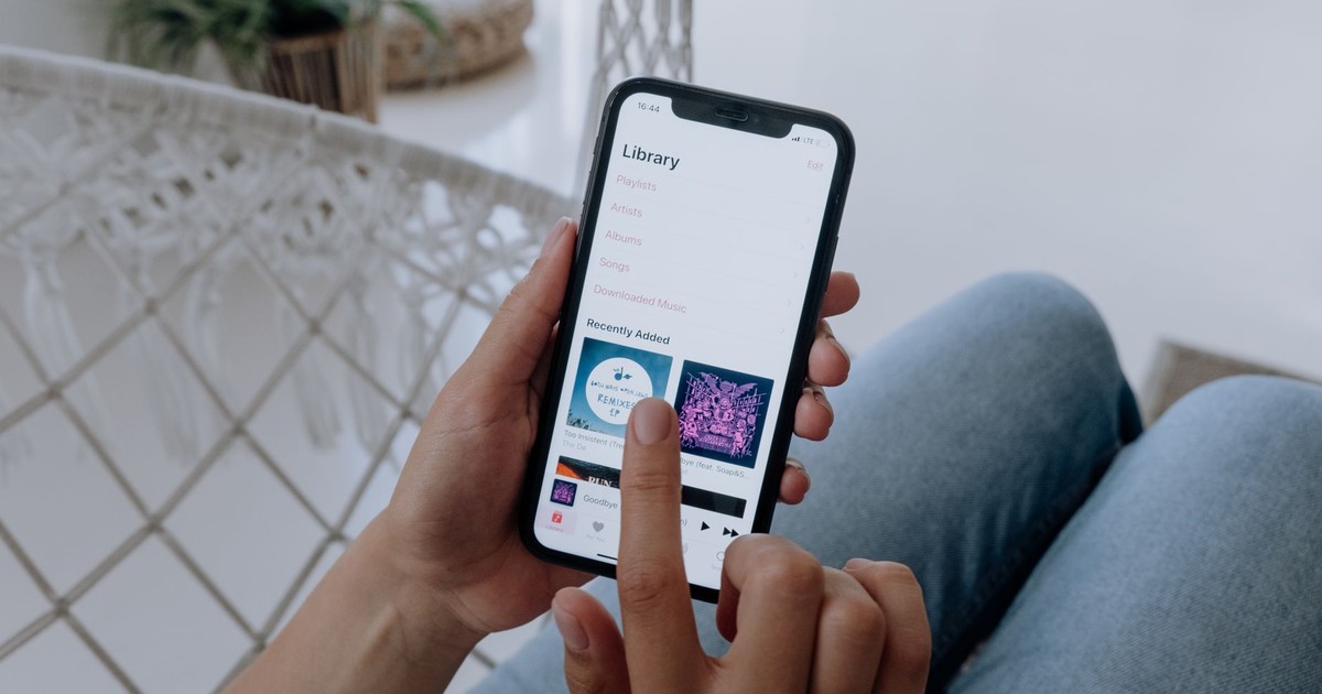 A person in jeans using a smartphone to browse a music app indoors.
