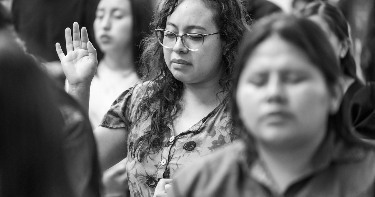 Black and white photo of a woman praying with others in Ciudad de México, capturing a serene moment.