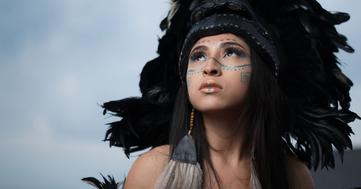 Woman wearing traditional feathered headdress and face paint, gazing upward.
