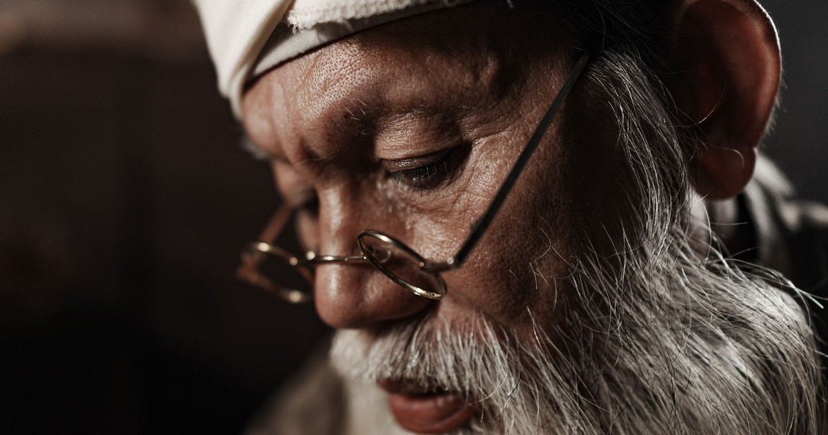 Close-up portrait of an elderly man wearing glasses and a white headscarf, deep in thought.