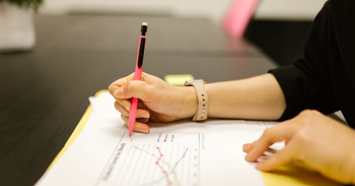 Person writing on a document with a pen, highlighting graph analysis.