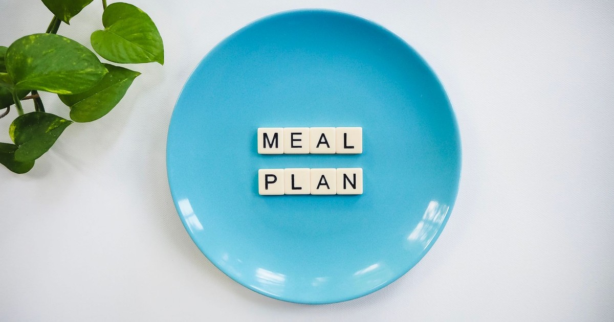 Innovative meal planning concept using alphabet tiles on a blue plate with green leaves.