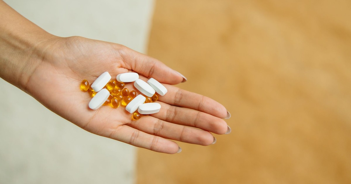 Close-up of a hand holding white pills and yellow capsules, symbolizing health and wellness.