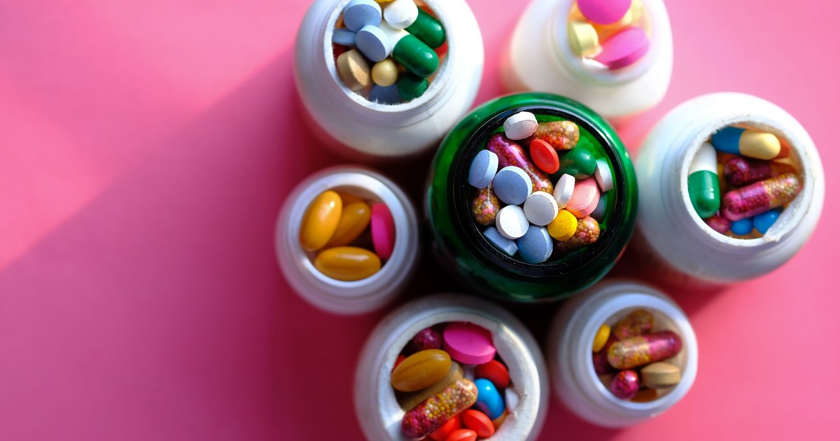 Top view of various medication pills and capsules in containers with bright pink backdrop.