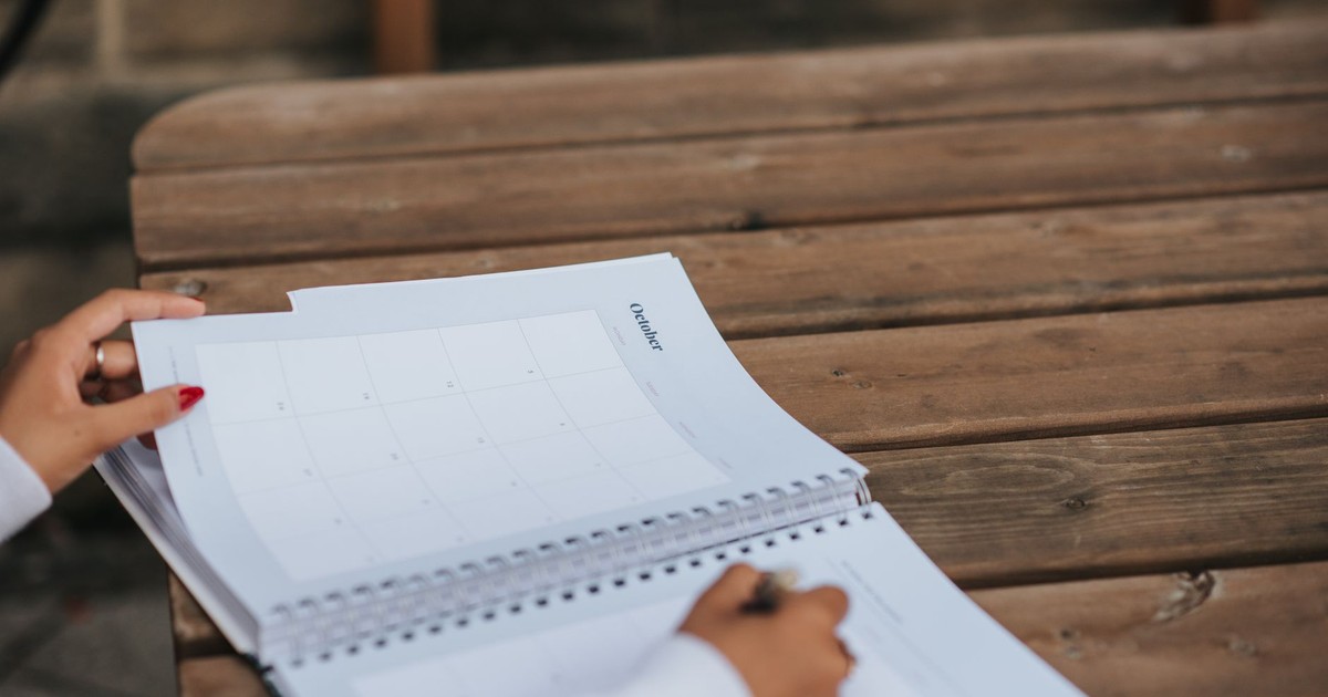 Crop anonymous female student writing in planner while sitting at wooden table in park