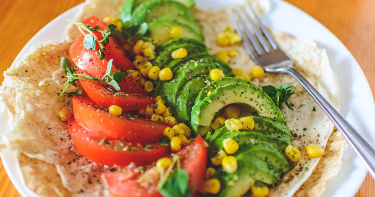 A vibrant salad with avocado, tomato, and corn on flatbread, topped with herbs, perfect for a healthy meal.