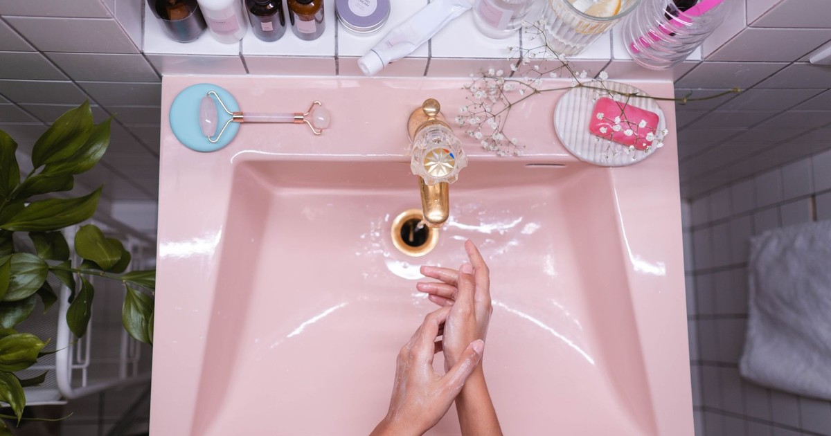 A stylish bathroom setup with skincare products and a person washing hands in a pink sink.