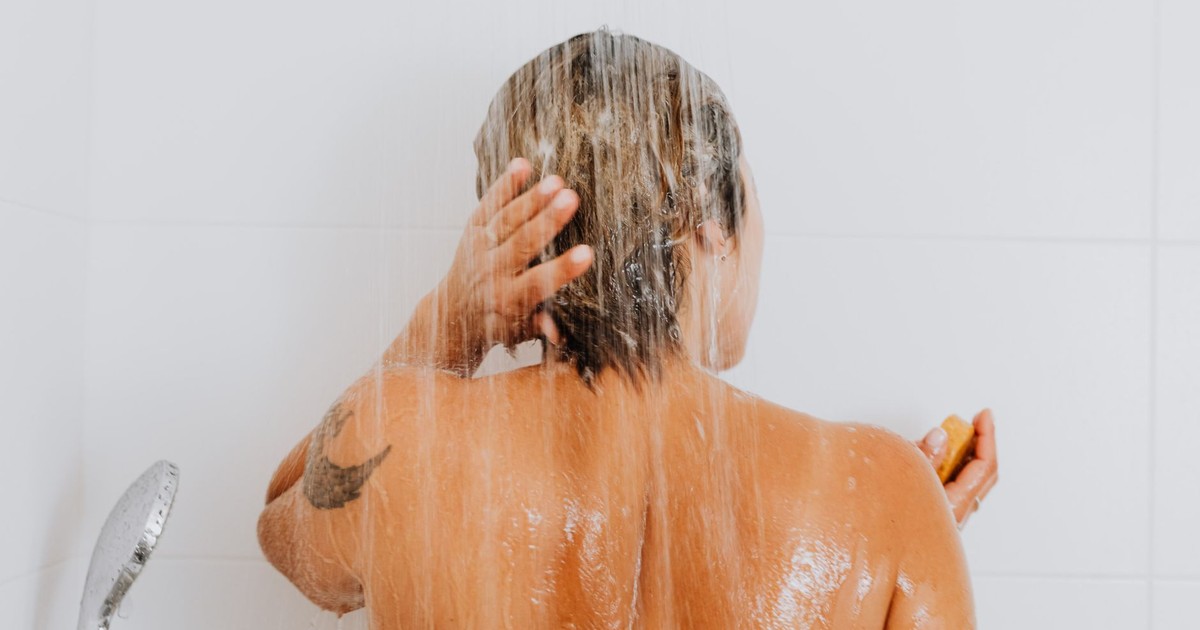 Rear view of a woman rinsing hair under shower, capturing an intimate and refreshing moment indoors.