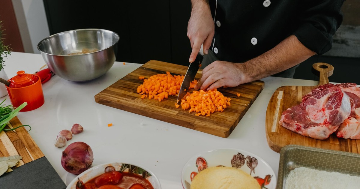 Chef chops carrots on a cutting board surrounded by fresh ingredients in a modern kitchen.