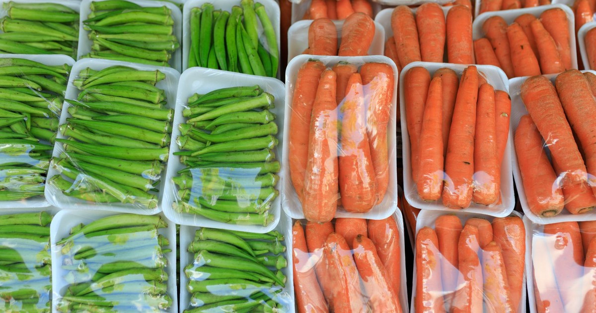 Assorted fresh okra and carrots neatly packaged in plastic trays at a market display.